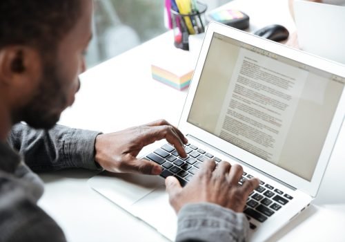 Cropped photo of serious young man sitting in office coworking. Looking aside using laptop computer. Focus on computer.